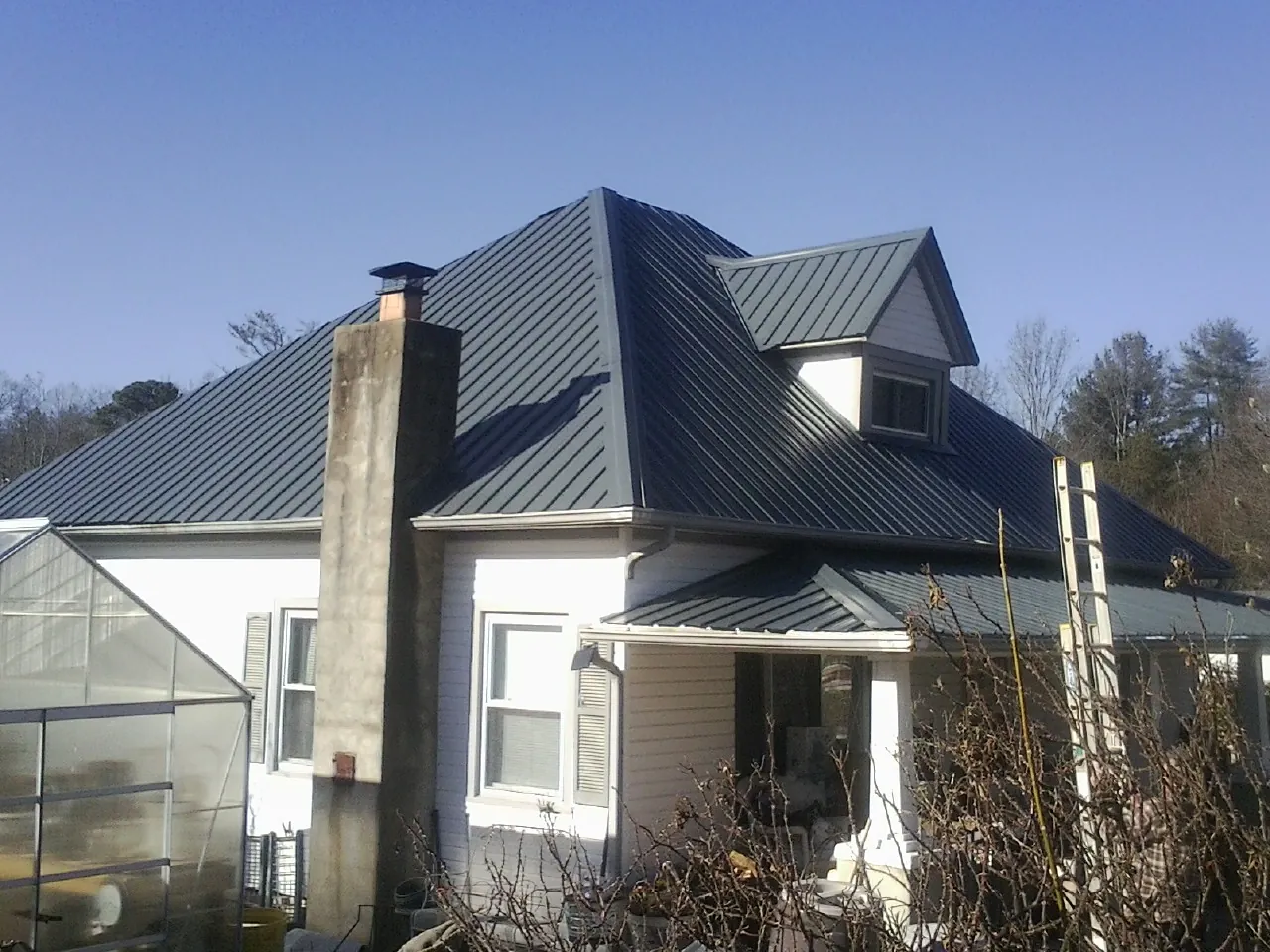 Dark blue standing seam metal roof on a white farmhouse with dormer — Slate & Tile Roof Repair by Roofing Brothers in Cambridge City