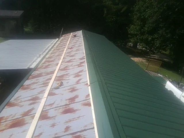 Old rusted panels beside newly installed green metal roofing — Wind Damage Roof Repair by Roofing Brothers in Cambridge City
