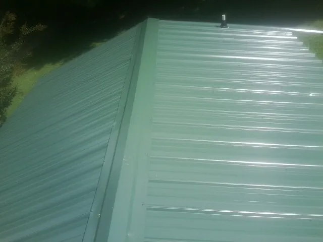 New green metal panels meeting at the ridge of a roof — Flat Roof Repair work by our crew in Cambridge City