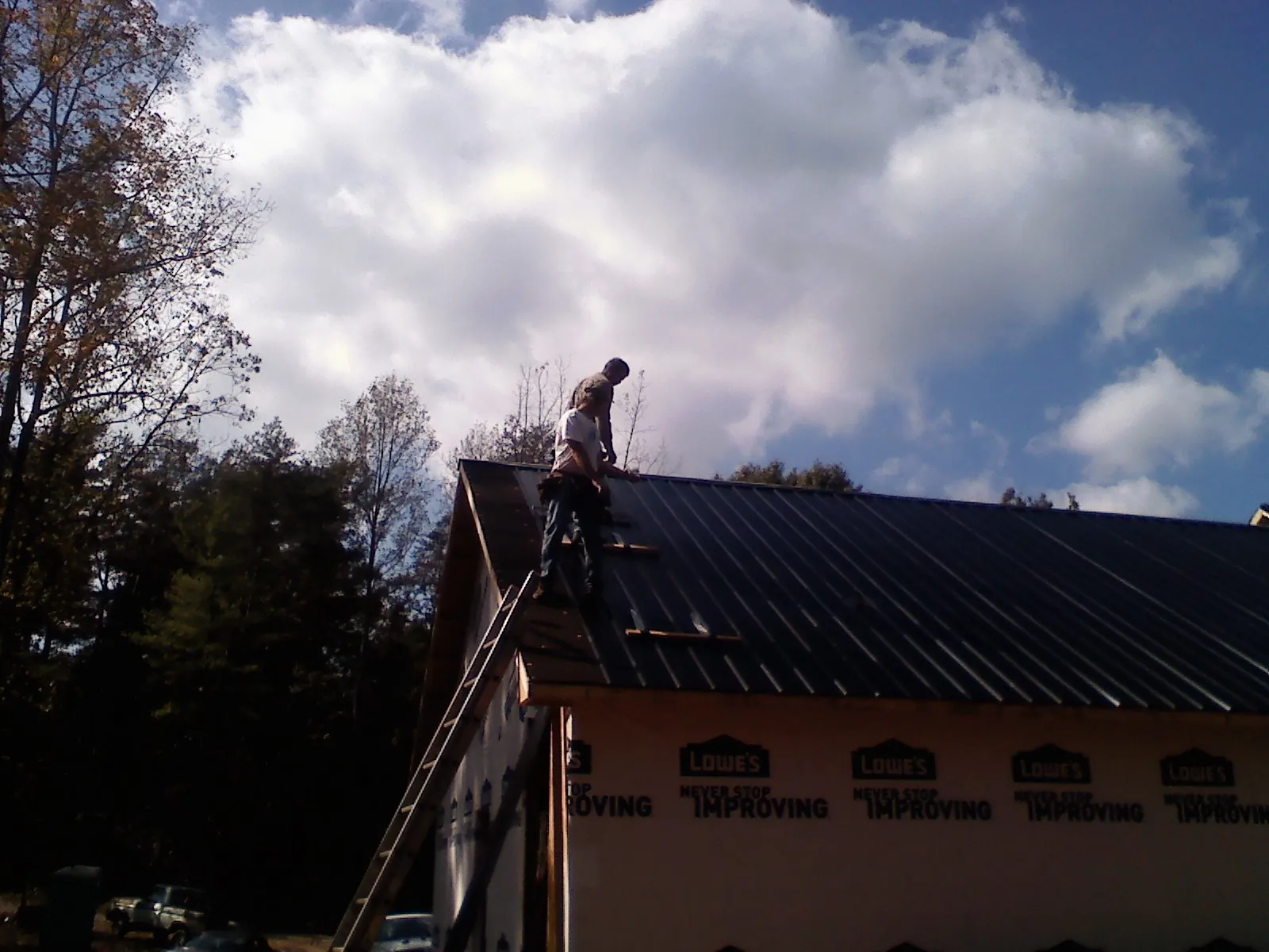 Roofer fastening dark metal panels high against a cloudy sky, from a Roof Inspection job in Cambridge City