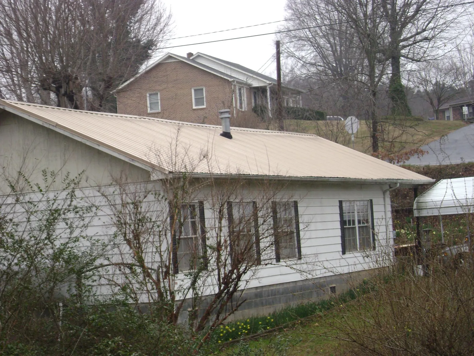 Tan metal roof on a white sided house set into a hillside — Commercial Roofing by Roofing Brothers in Cambridge City