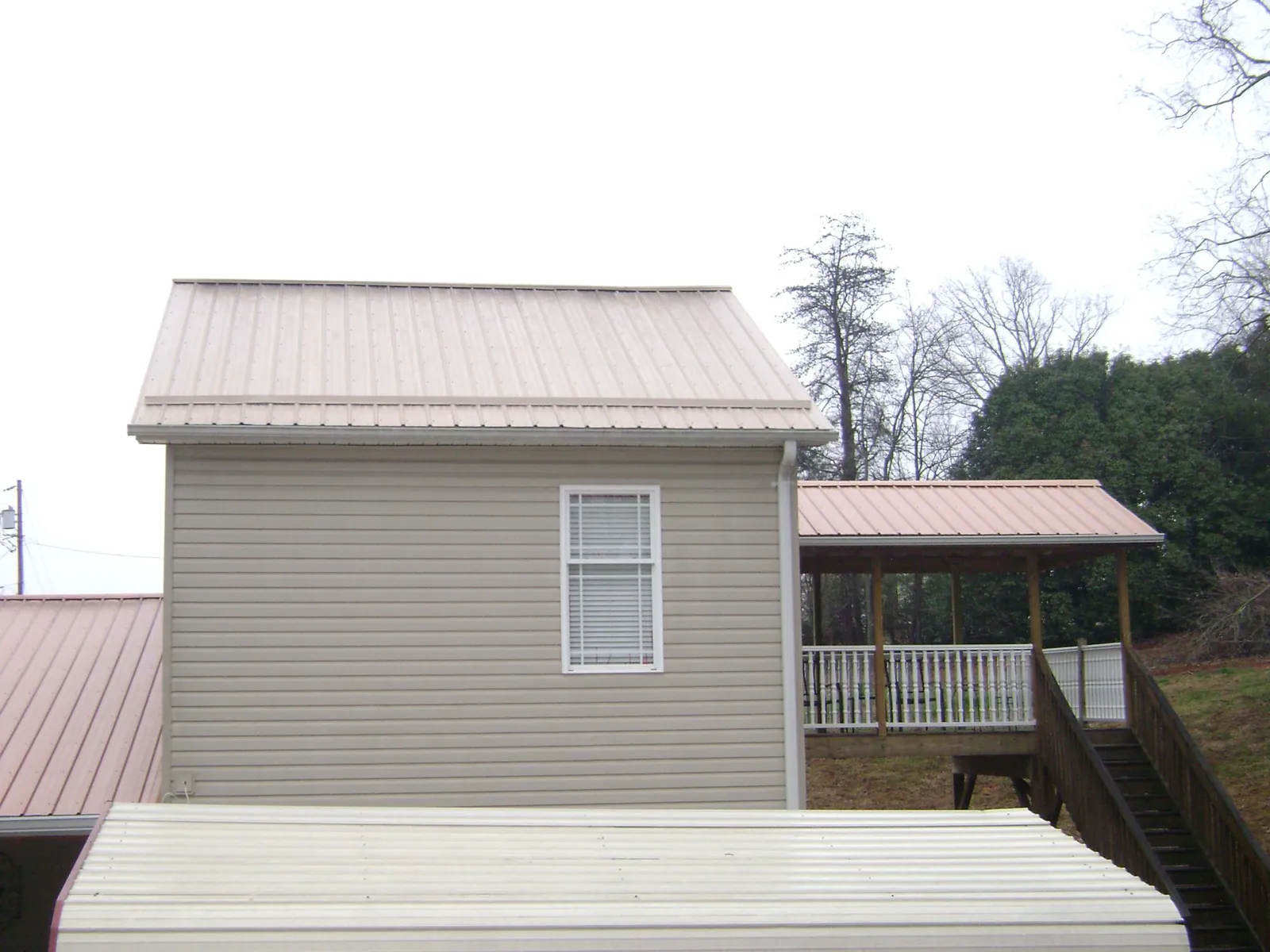 Tan metal roofs on a two story addition and attached porch, from a Roof Replacement job in Cambridge City