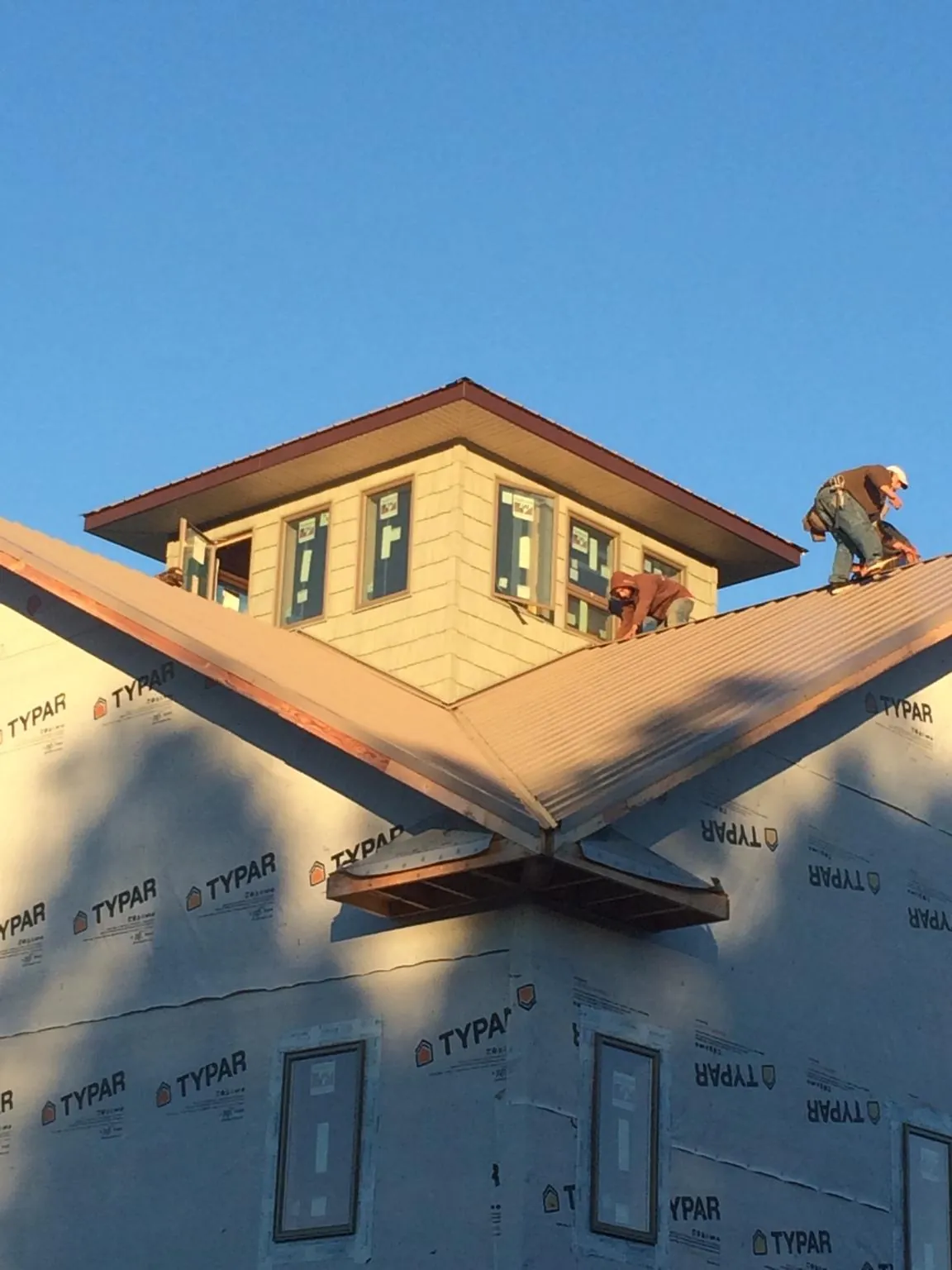Roofers working around a rooftop cupola on a new metal roof at sunset — Roof Waterproofing in Cambridge City by Roofing Brothers